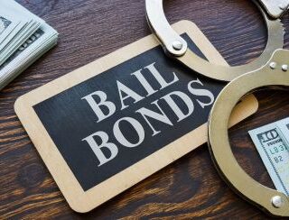 a bail bonds card, handcuffs and cash sitting on a desk used for Bail Bonds and Bail Bond Loans in Houston Gardens, TX