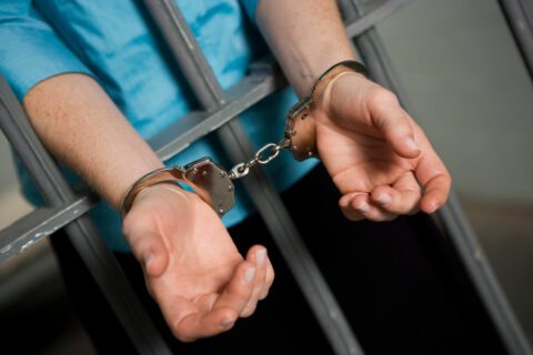 Handcuffed hands through jail bars needing a bail bond in River Oaks