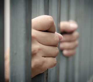 Hands gripping jail bars waiting for 24 hour bail bonds in Humble